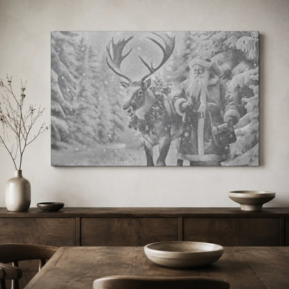 A large black and white canvas wall art print depicting Santa Claus and a reindeer in a snowy forest, displayed on a light beige wall above a dark wood console table with decorative bowls and a vase.